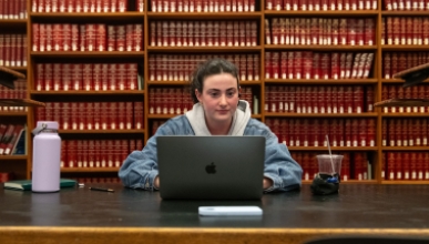 An Occidental College student studying intently with her laptop against a backdrop of thick library books