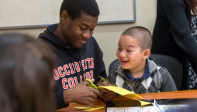 An Occidental College male student helps a young child with a paper craft project