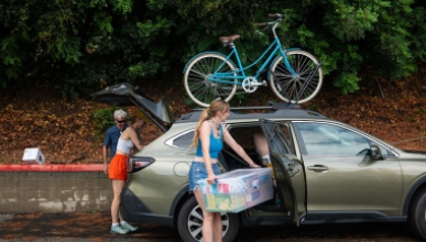 a student unloading her belongings from a car with a bright blue bike strapped to the top