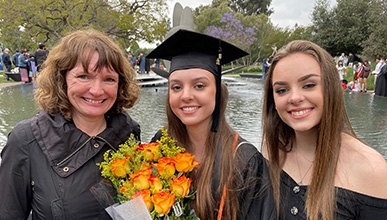 Oxy parent and sibling flank graduating Oxy student wearing graduation cap, with Gilman Fountain in background