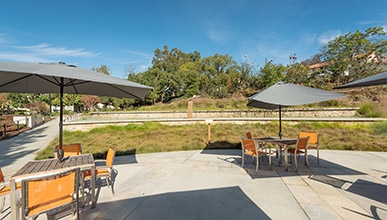 Umbrella shaded tables and chairs on the HCC patio in the foreground with a beautiful blue sky in the background