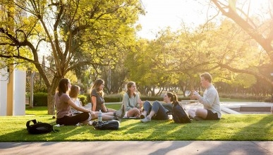 A group of students sit chatting in a circle on the quad at sunset