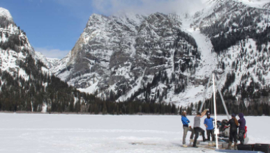 a group of researcherscollecting samples on a frozen alpine lake surrounded by snow-covered mountains,   representing the Environmental Science department at Occidental College (Oxy).