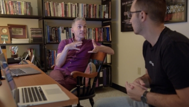 Faculty member Broderick Fox speaks to student Brendan Galbreath in an office full of books