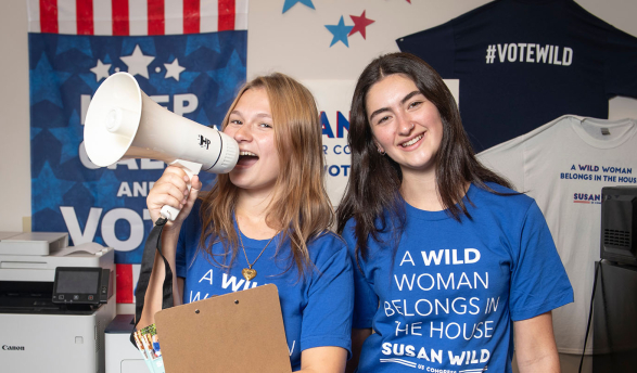 Two female Occidental students stand together with clipboards, a megaphone and blue campaign tshirts