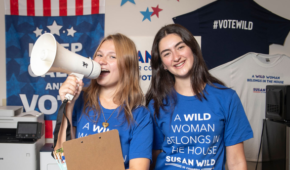 Two female Occidental students stand together with clipboards, a megaphone and blue campaign tshirts