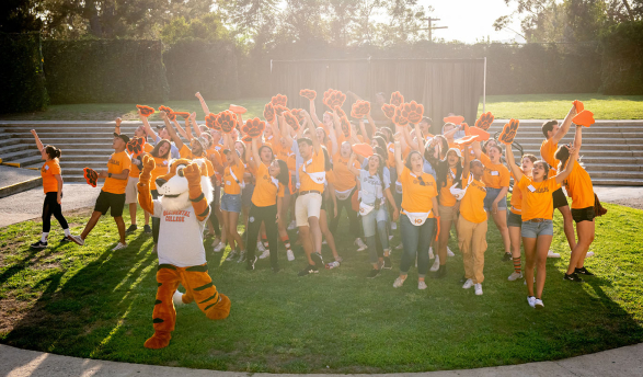 A crowd of Occidental College O-Team orientation leaders, cheering in a green field with Oswald in front