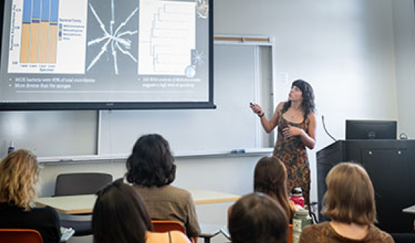 a student giving a lecture looking up at a projection screen with students looking on