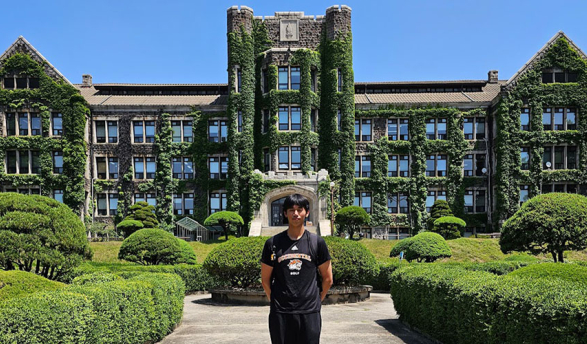 Hunter Leong stands in front of a university building in Korea whose walls are covered by moss