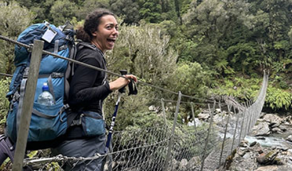 a young woman with a backpack about to cross a stream