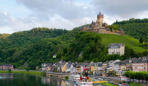 a beautiful hillside topped with a European castle next to a river