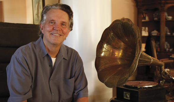 Mike Curb in a grey shirt sitting next to a gold grammophone