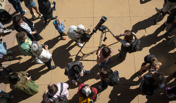 A group of Occidental College staff and students looking at the solar eclipse through a telescope, shot from above