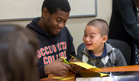 An Occidental College male student helps a young child with a paper craft project