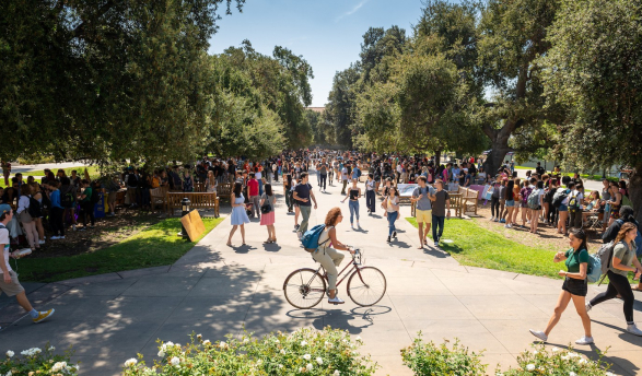 a girl on a bike rides across the Quad full of students
