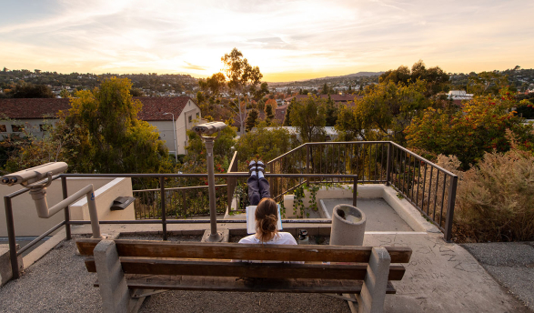 A view of a student on a bench overlooking campus from above at sunset