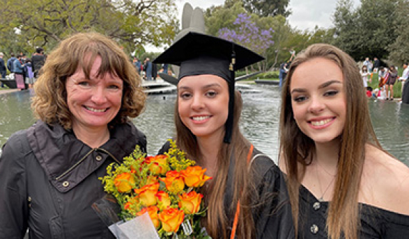 Oxy parent and sibling flank graduating Oxy student wearing graduation cap, with Gilman Fountain in background