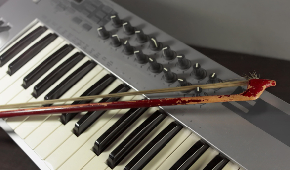 an electronic keyboard controller with a violin bow resting on its keys