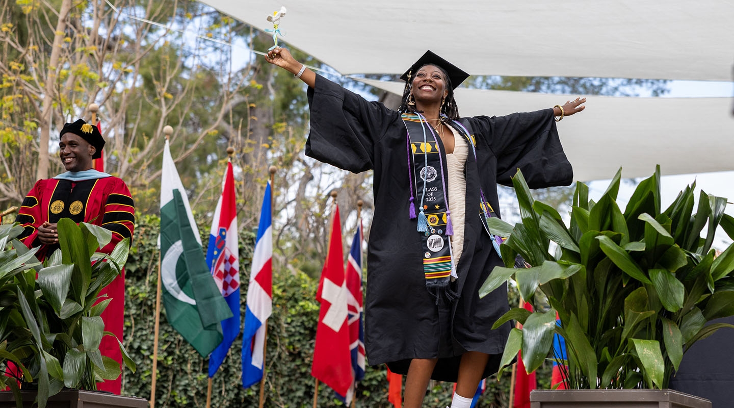 An Occidental College graduate crossing the stage and jumping joyfully in to the air