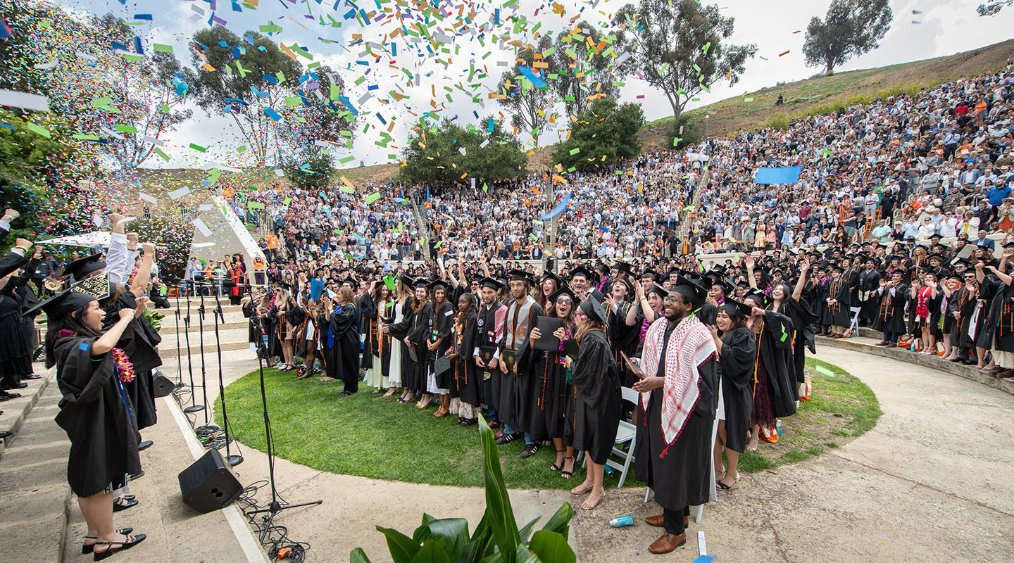 A scene at Commencement in the Hillside Theater of graduates standing in their caps and gowns amid colored confetti in the air