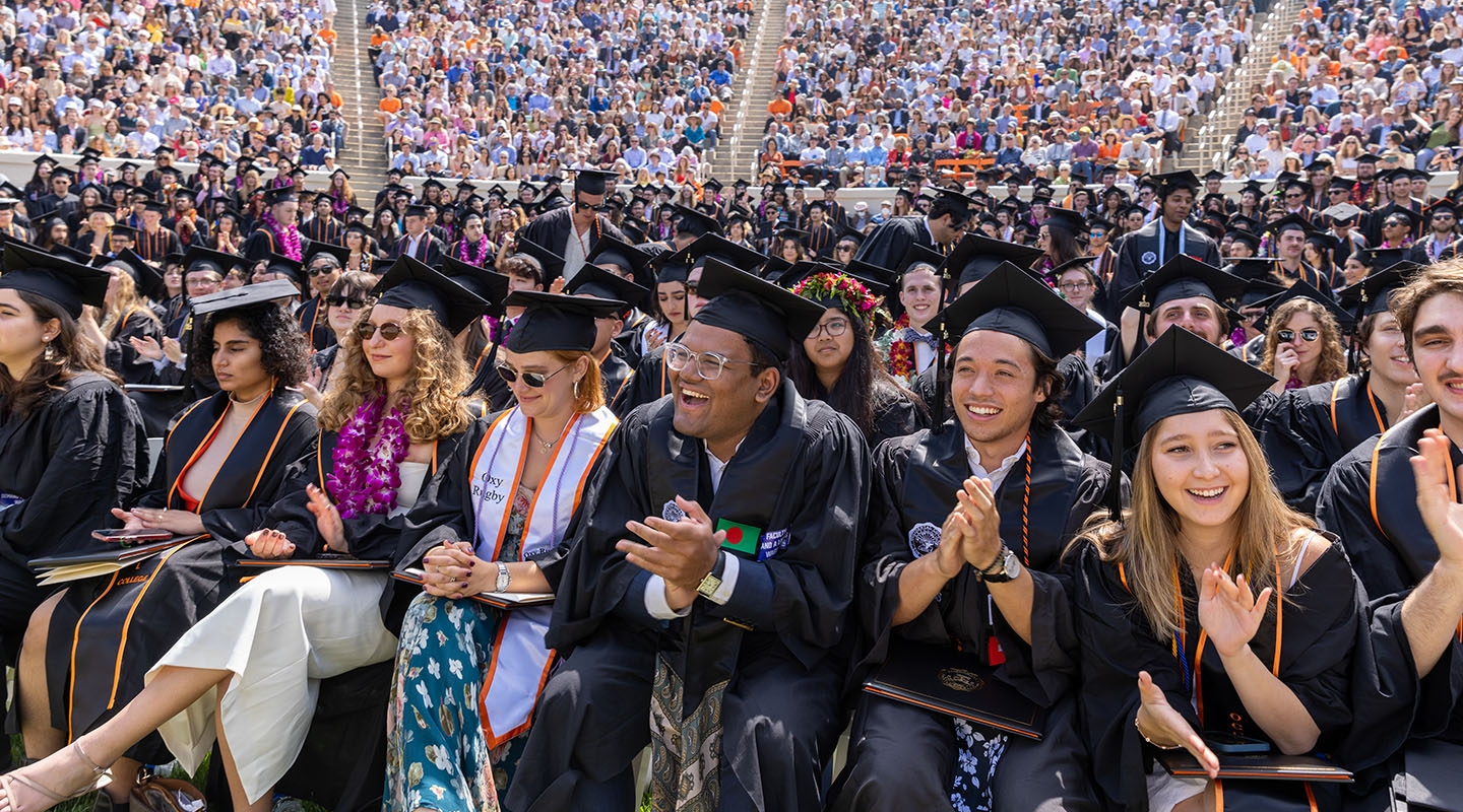 a view of the audience at Commencement with graduates in front smiling