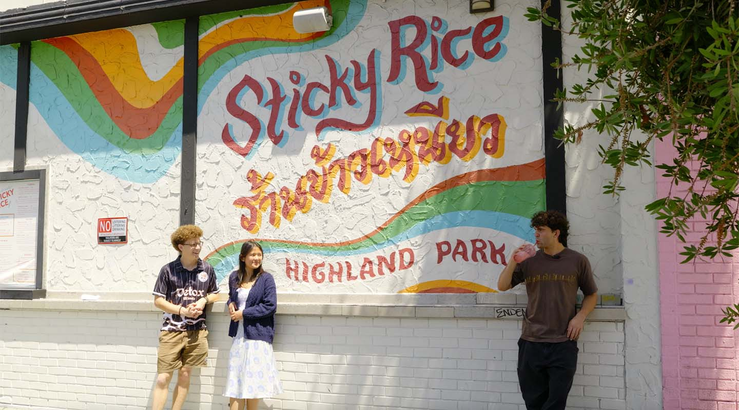 Three Occidental College students standing in front of the wall of the restaurant Sticky Rice