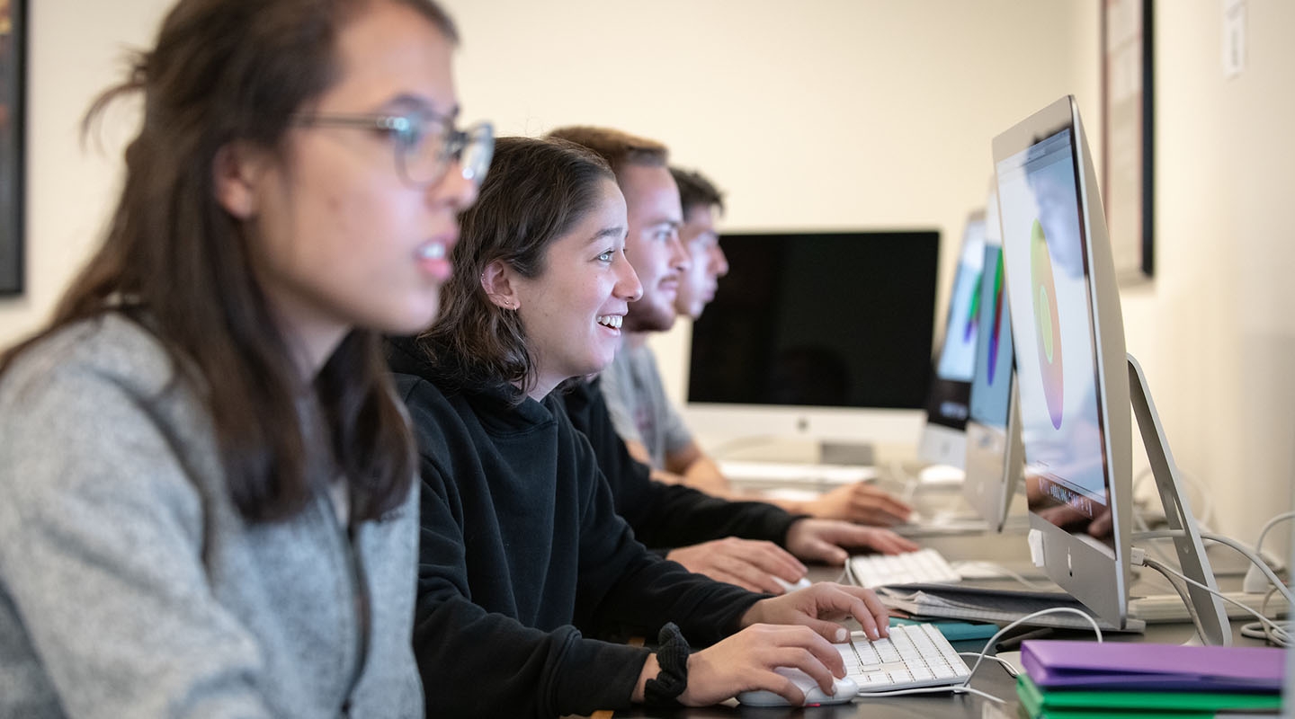 students sitting in front of a row of computers