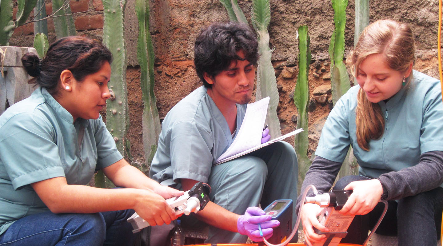 Three scientists sitting together using instruments to measure air quality in Peru