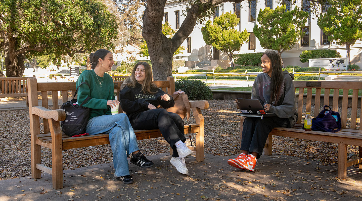 Three Occidental College students talking together on benches on the campus Quad