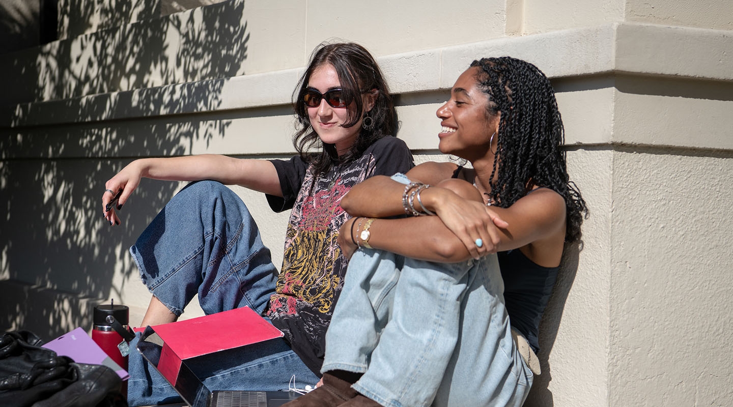 Two Occidental College students relaxing in the sun next to the library building