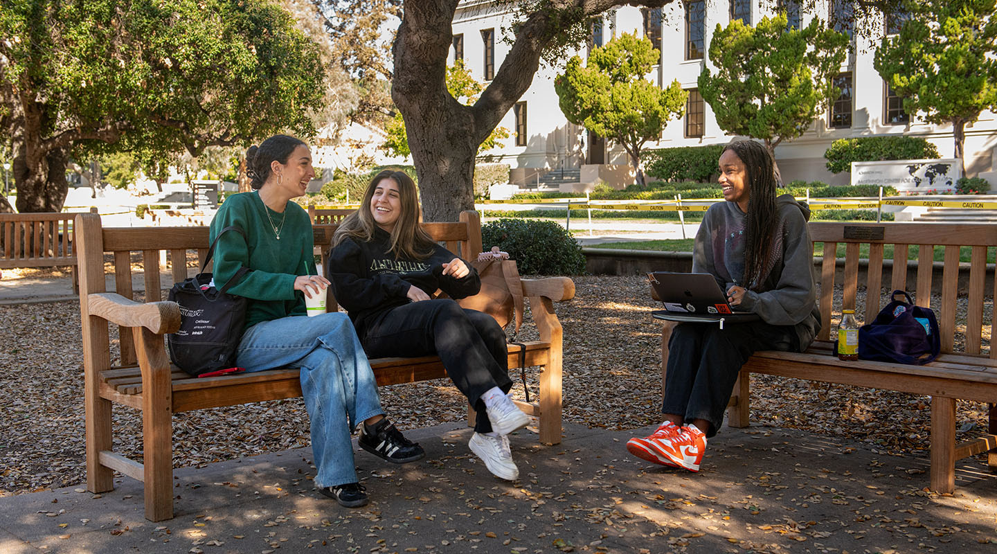 Three Occidental students sitting and talking on benches in the Quad on campus