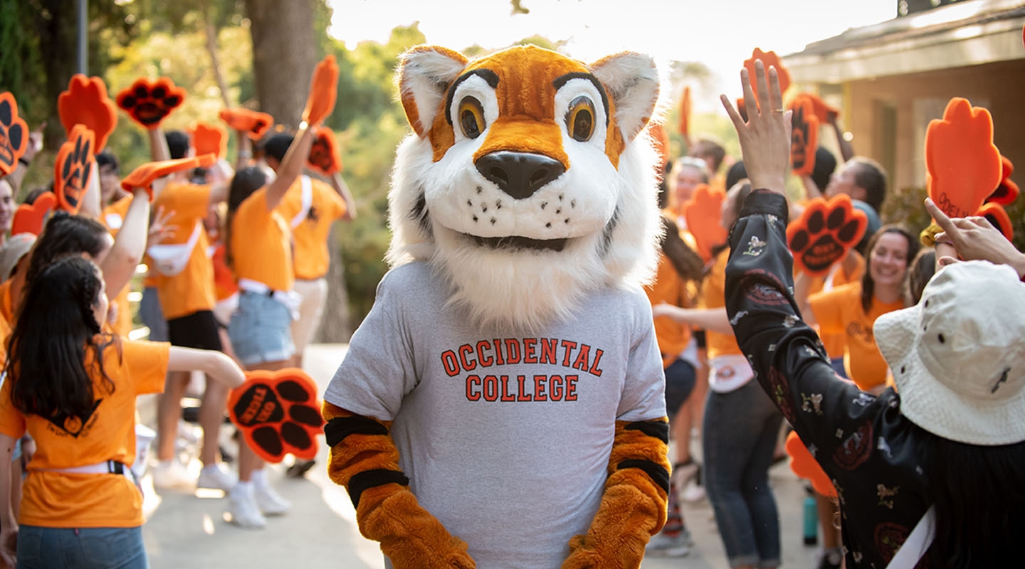 Occidental College's mascot, Oswald, stands smiling in the midst of happy Oxy students