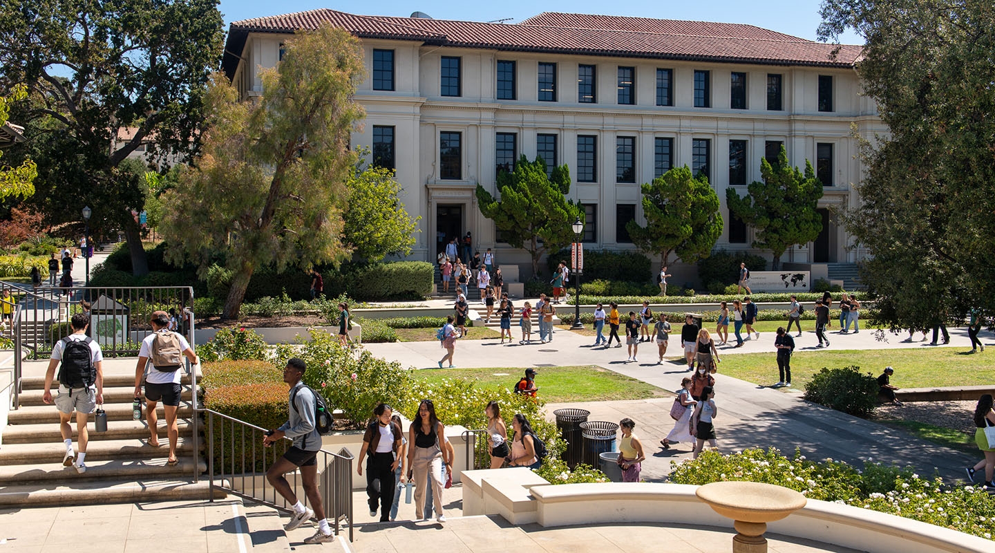 A view of Occidental College students on campus, entering Johnson Student Center and walking up steps with Fowler Hall in the background.
