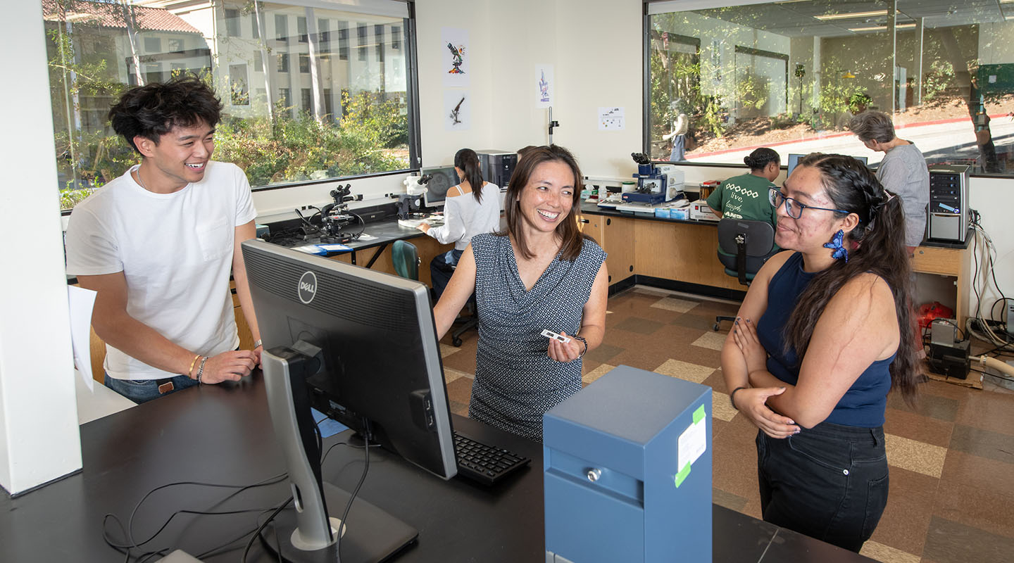 Occidental students flank their professor Dr. Okamura in the biology lab, smiling and laughing