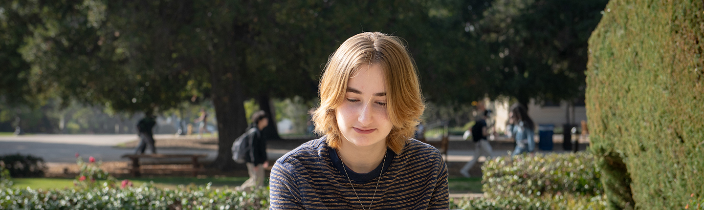An Occidental College student sits at an outdoor table looking at her laptop.