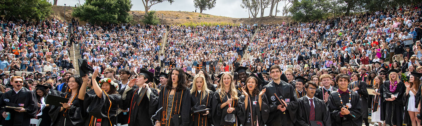 Occidental students standing in black caps and gowns in the Remsen Bird Hillside Theater, celebrating