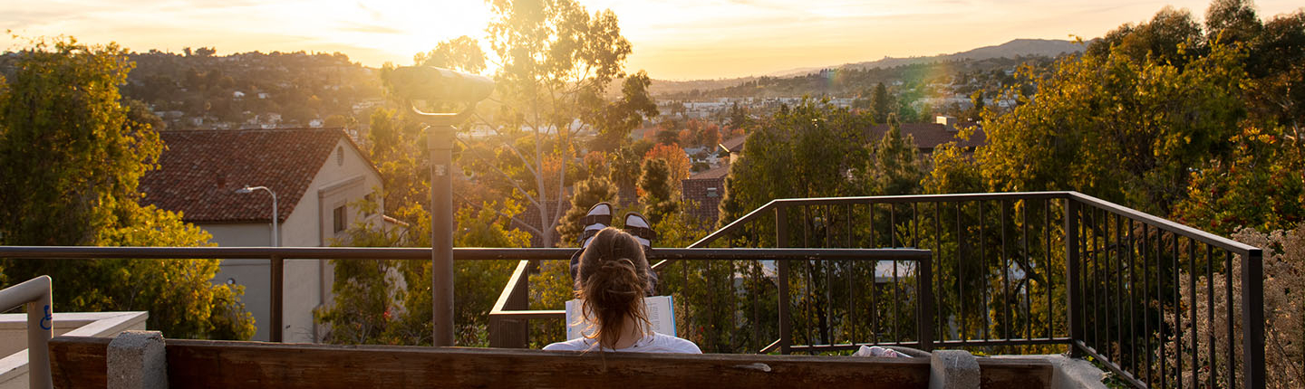 an Occidental student reading a book on a bench on campus as the sun sets