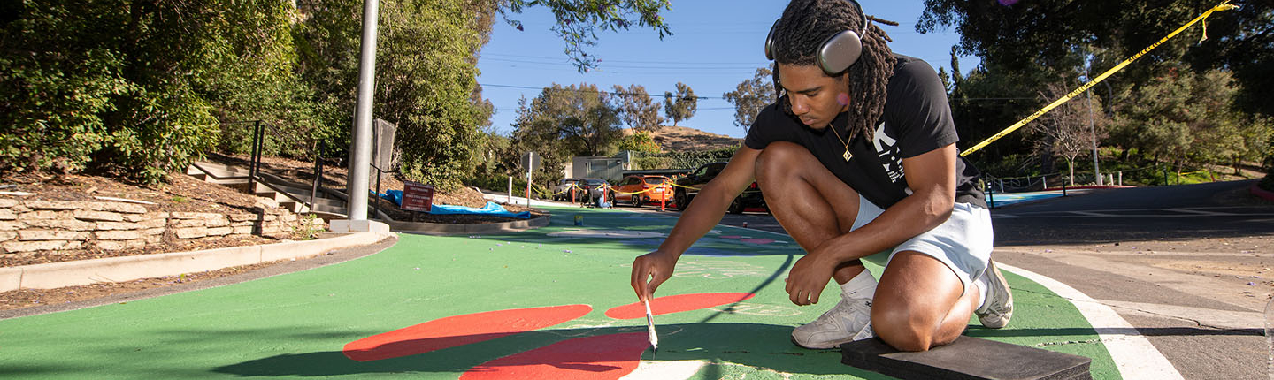 An Occidental College student paints a mural on a road on upper campus