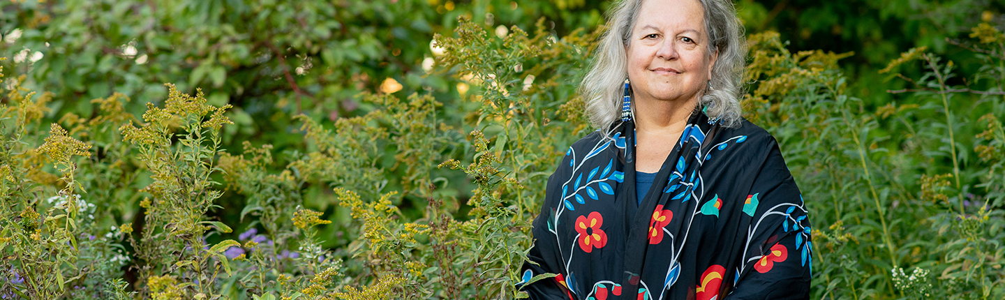 Robin Wall Kimmerer photographed outdoors in front of a green setting with wildflowers