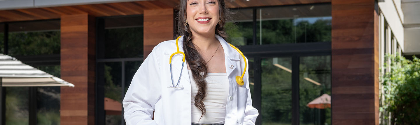 A young Oxy alumna stands outside the HCC with a medical coat and stethiscope