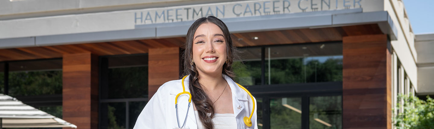 A young Oxy alumna stands outside the HCC with a medical coat and stethiscope