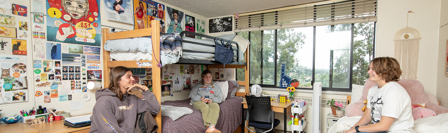 three students chatting together in a decorated dorm room