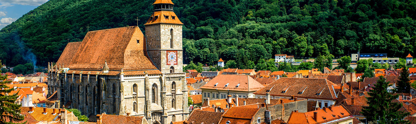 A quaint Romanian village with orange-colored roofs and a steeple in the middle against a lush green hillside