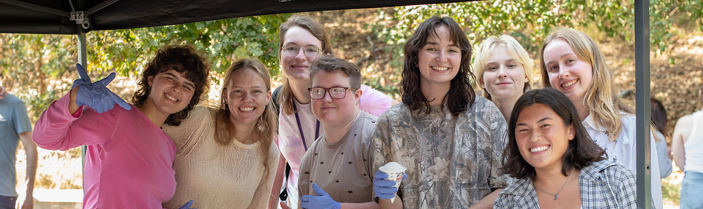 A happy group of Occidental College students posing together at a snow cone assembly table