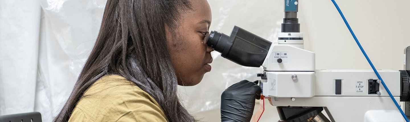 Daisy Ademoye looking into a powerful microscope in the Mind and Brain lab