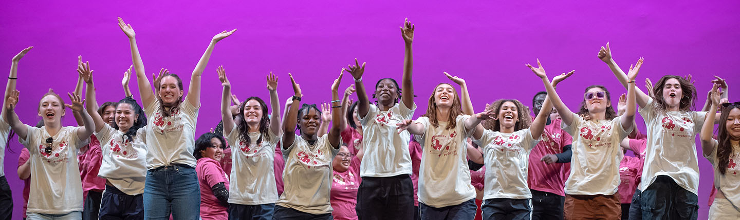 Oxy students on stage, arms up and smiling as they perform in Dance Pro