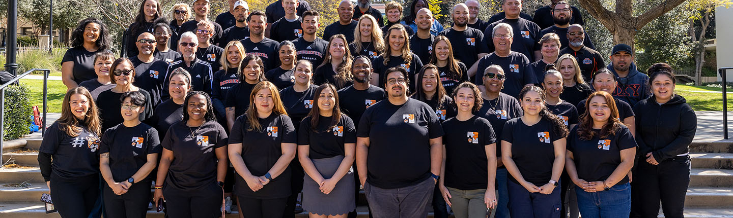 A large group of Student Affairs staffers standing on the steps on campus in black tshirts