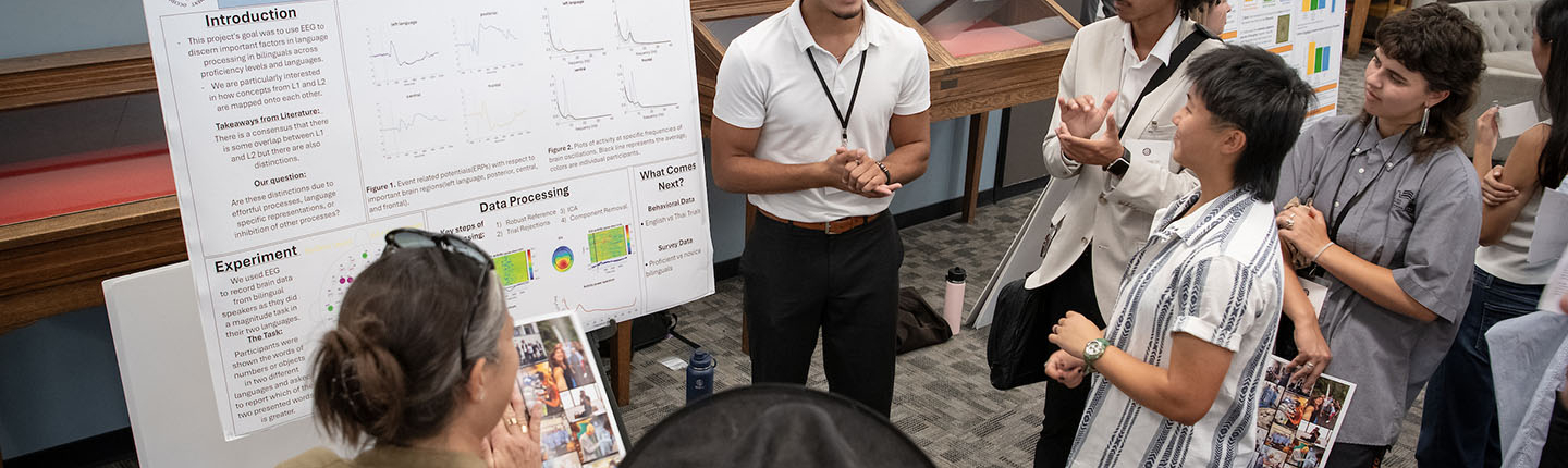 a group of Occidental College students stands around a male student giving a poster presentation about his research
