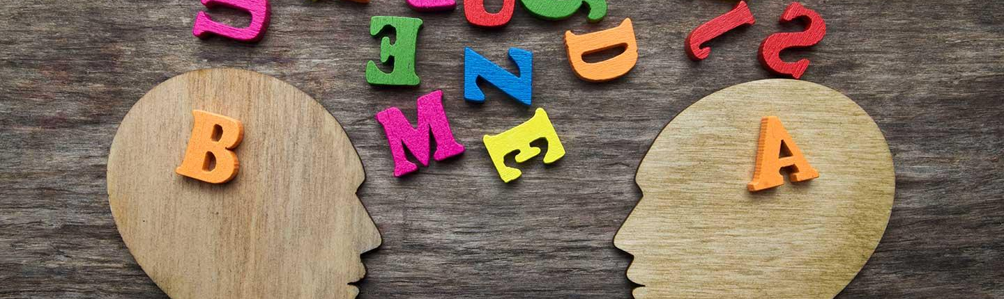 two wooden head cutouts and colored jumbled letters representing different individuals attempting to communicate