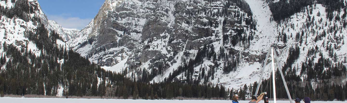 a group of researcherscollecting samples on a frozen alpine lake surrounded by snow-covered mountains,   representing the Environmental Science department at Occidental College (Oxy).